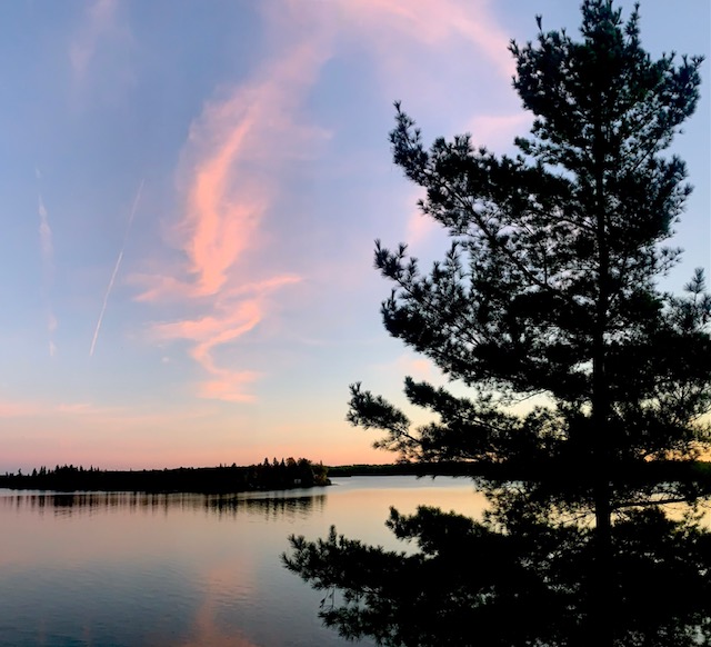 Sunset over a calm Northwestern Ontario lake with pine tree silhouettes